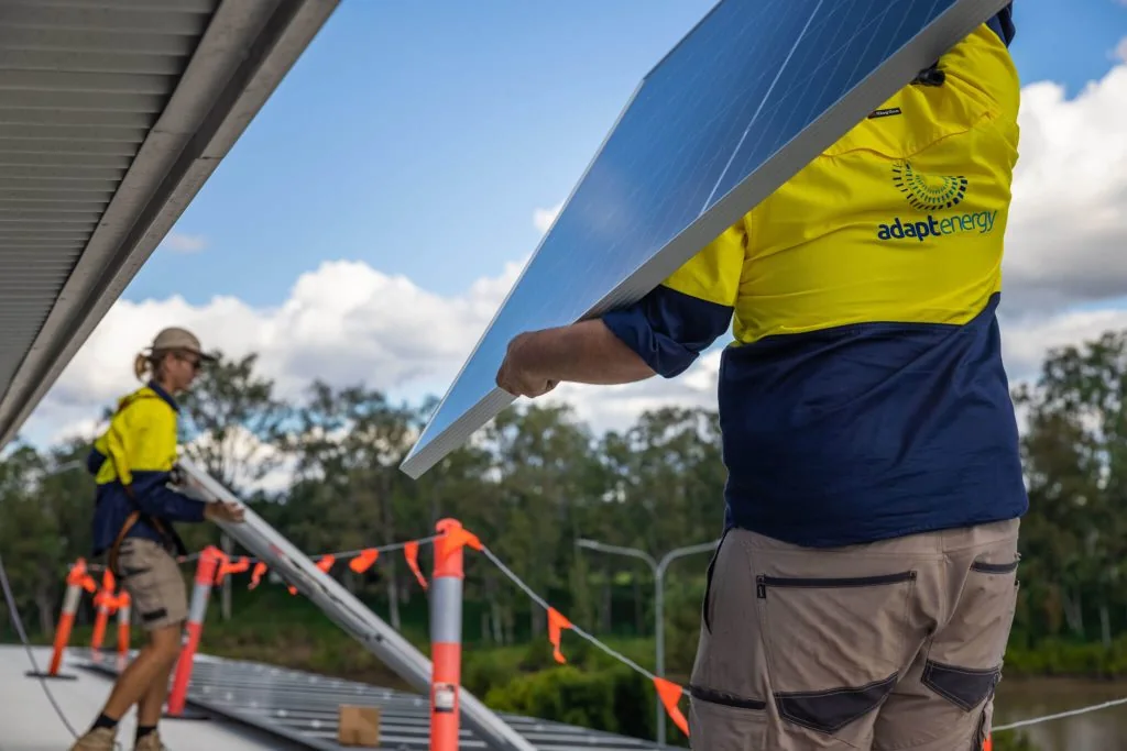 Two of our installers on a metal roof, lifting a solar panel into place inside a taped-off work zone