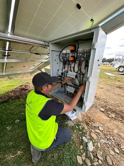 One of our electricians wiring a combiner box beside a ground-mounted solar array